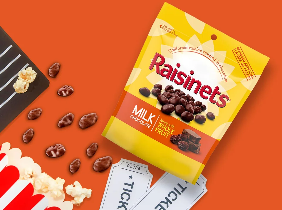 A Raisinets milk chocolate resealable bag with popcorn and movie tickets
