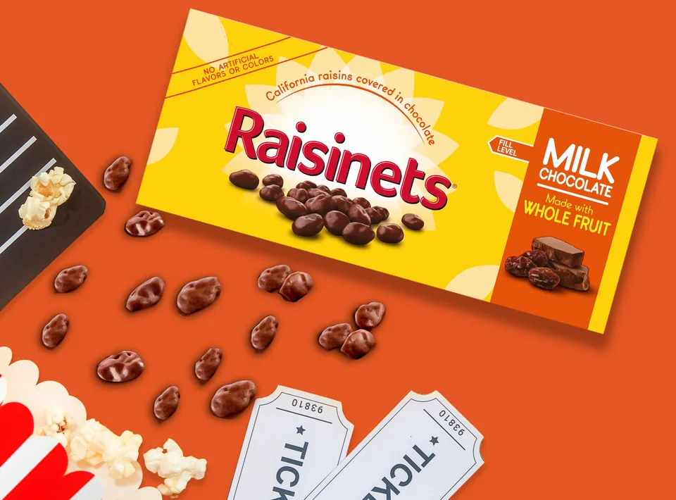 A Raisinets milk chocolate theater box with popcorn, movie tickets and loose chocolate-covered raisins
