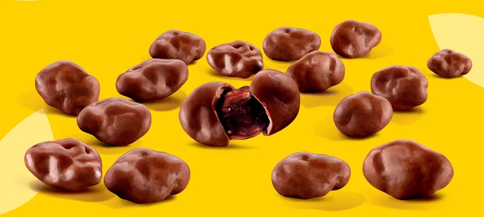 Loose milk chocolate covered raisins, one bitten open to show the raisin